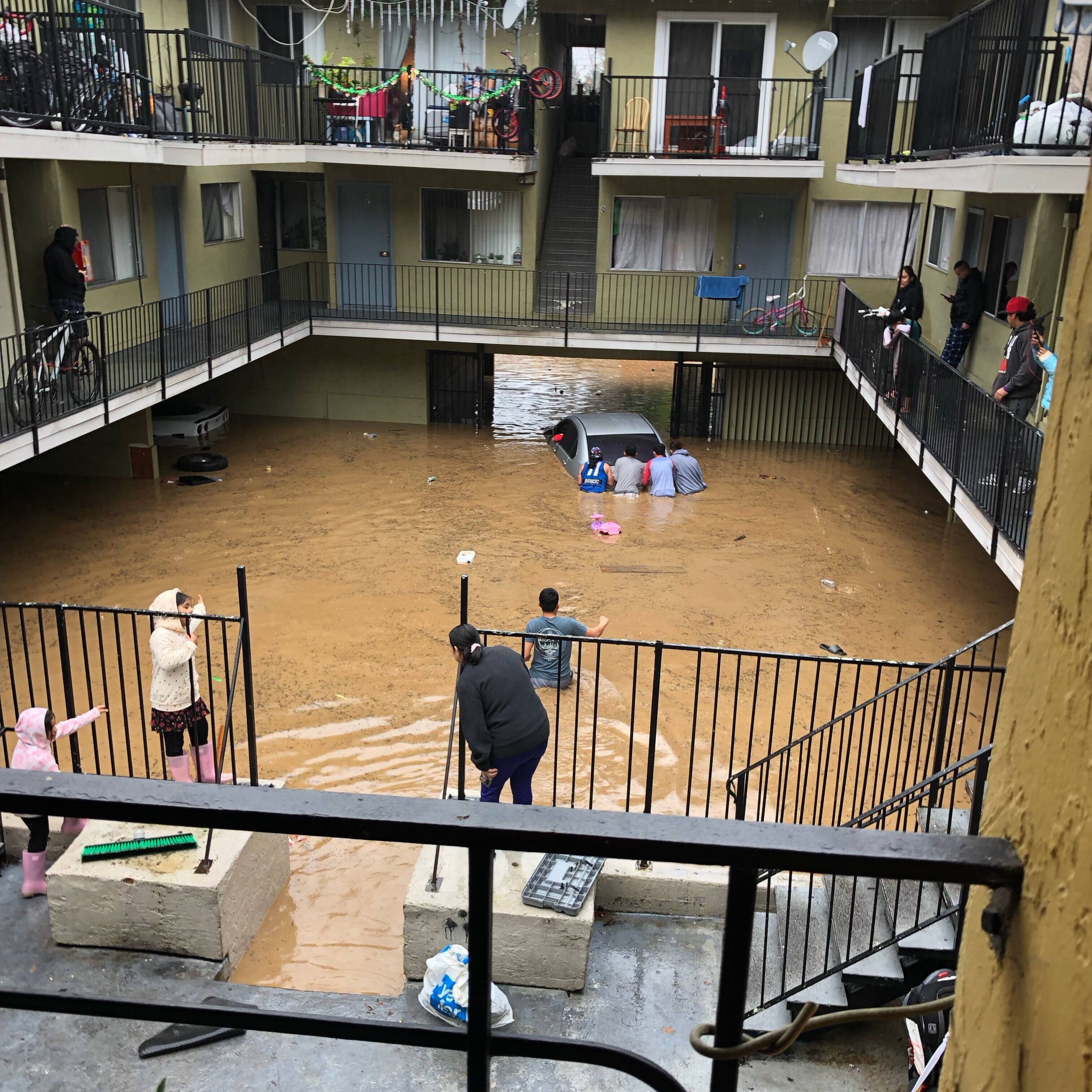 Flooded lower level of apartment building. Muddy waters with people pushing a truck